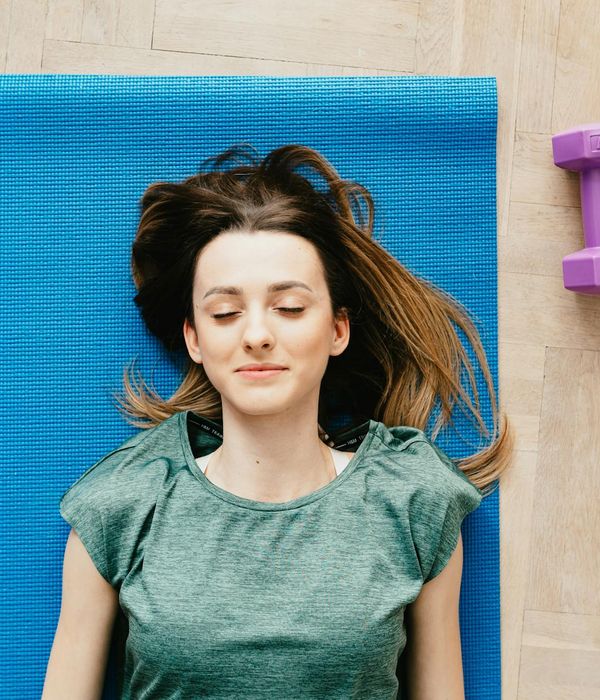 Smiling woman stretching gently on a yoga mat in a sunlit room.